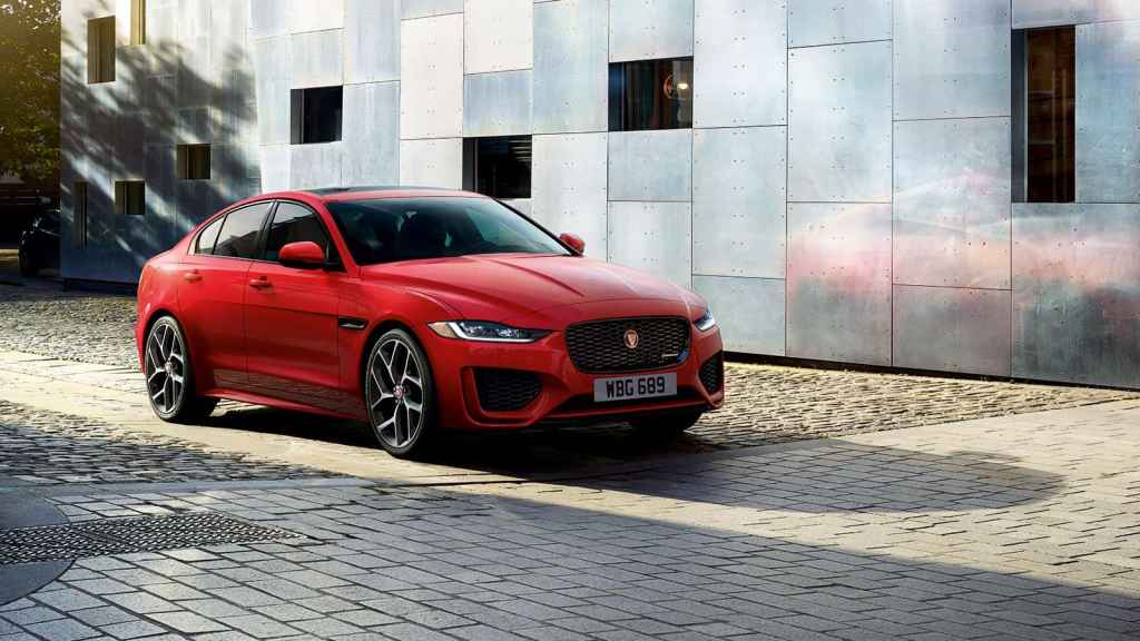 A red 2020 Jaguar XE sedan moves over a brick roadway by a building.
