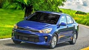 a blue Kia Rio driving on a scenic country road