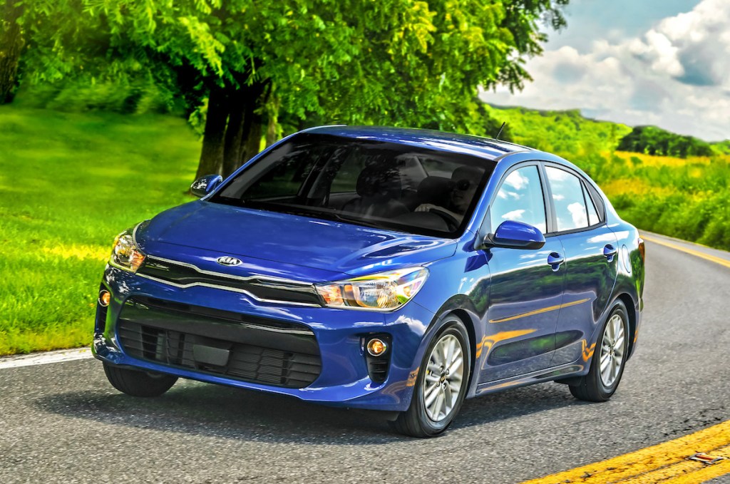 a blue Kia Rio driving on a scenic country road