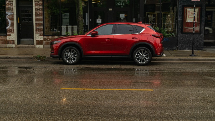 The side view of a red 2020 Mazda CX-5 Signature AWD on a rainy city street