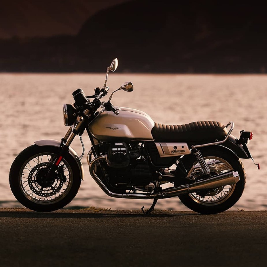 A white-tanked 2020 Moto Guzzi V7 III Special in front of a body of water at sunset