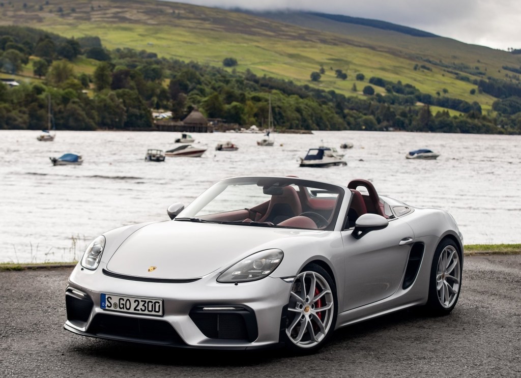 A silver 2020 Porsche 718 Spyder in front of a boat-filled lake