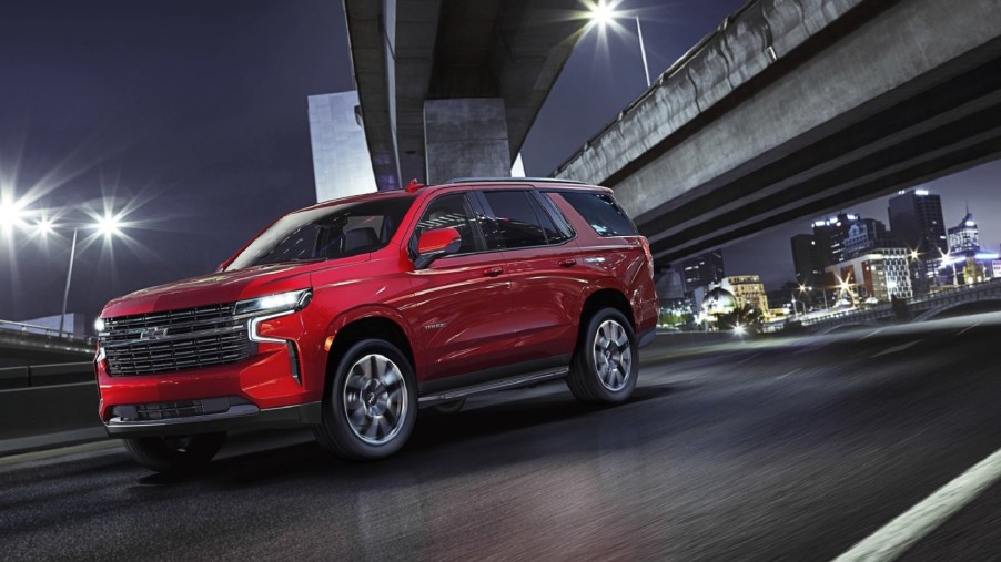 A red 2021 Chevrolet Tahoe drives on a city's highway at night
