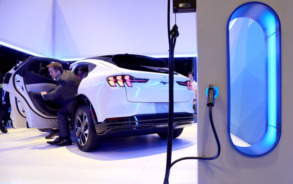 The rear of a white Ford Mustang Mach-E sits by an electric charging station.