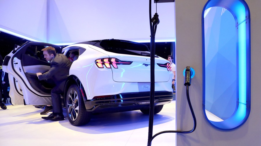 The rear of a white Ford Mustang Mach-E sits by an electric charging station.