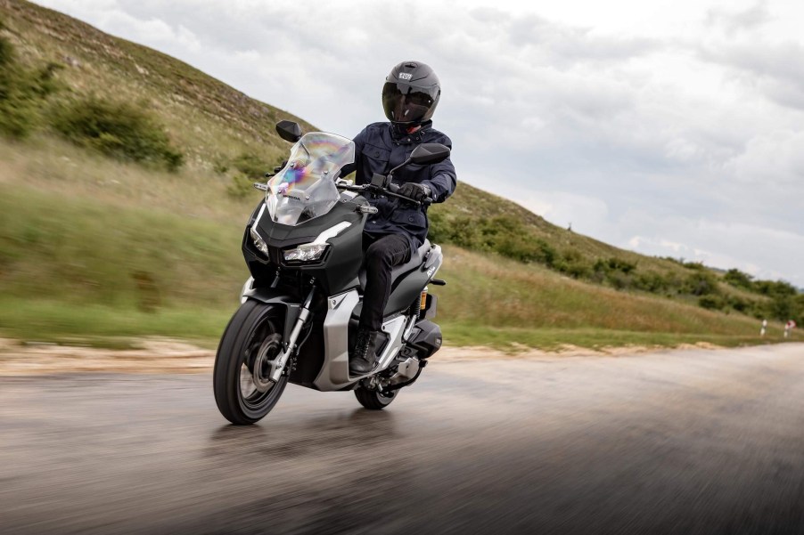 A black 2021 Honda ADV150 rides down a wet road