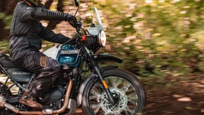 A rider guides a blue-and-white 2021 Royal Enfield Himalayan through a forest