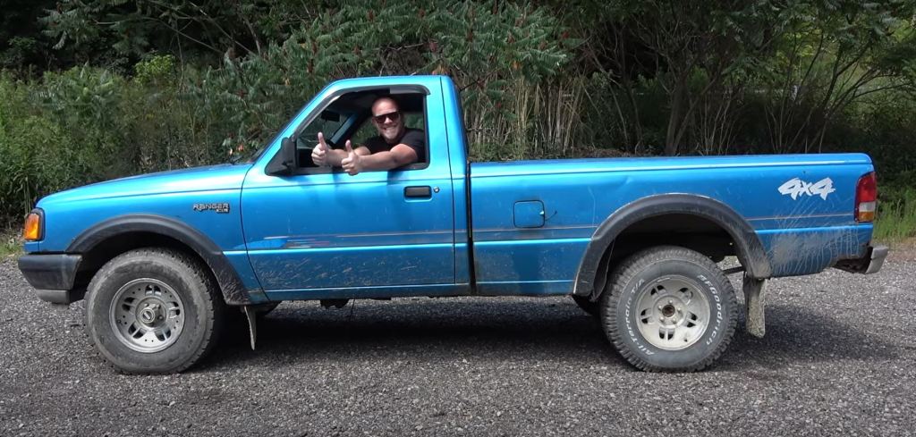 A man gives the thumbs up through the side window of a blue Ford Ranger pickup.