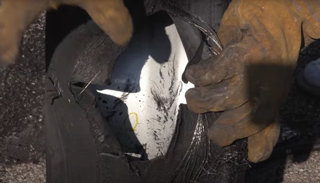 A worn tire has a large hole in it from a blowout.