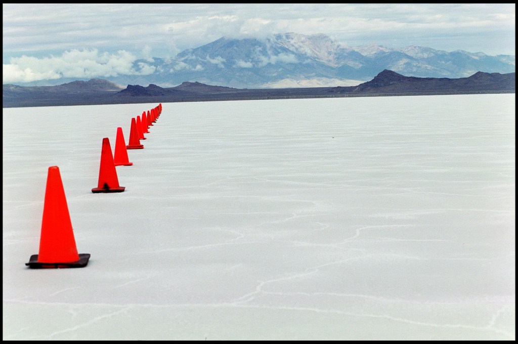 A flat white long field dissappears to the base of mountains in the background. One side is lined with traffic cones set for competition.
