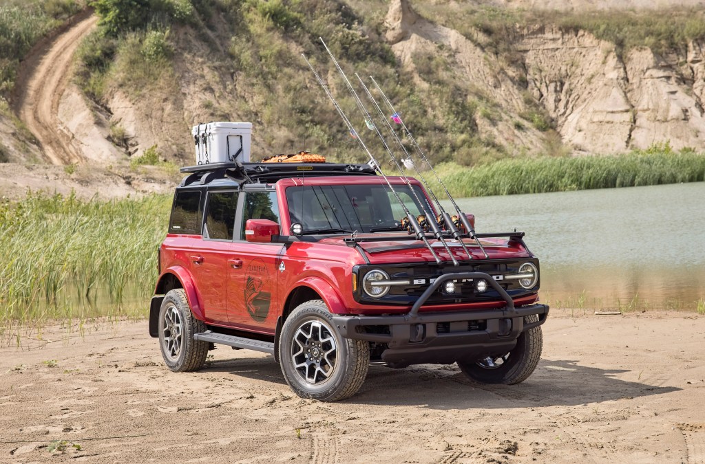 A red, four-door, 2021 Ford Bronco has the front top folded back and a custom fishing rod holder mounted on its hood. 