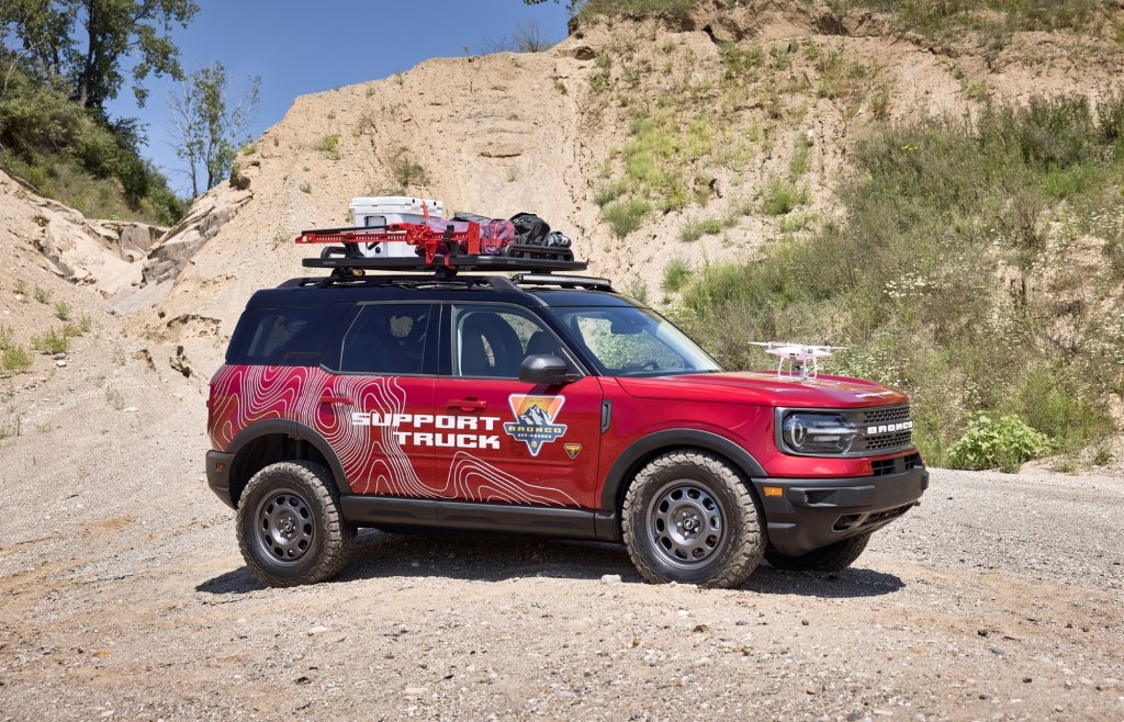 A red SUV with a roof rack and a lift kit traverses loose gravel.