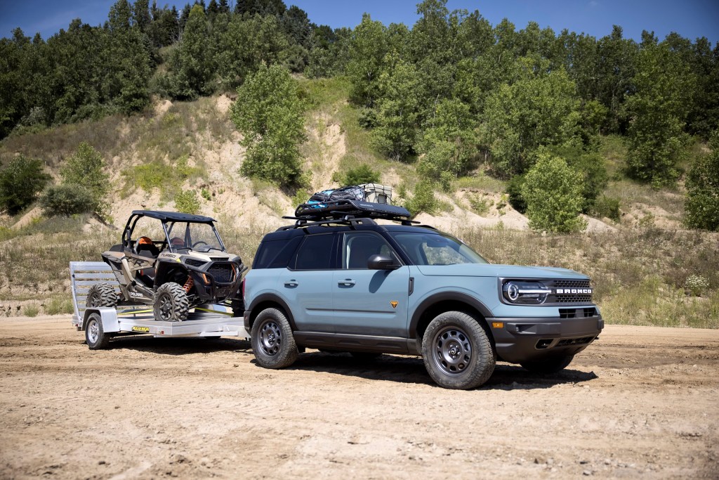 A gray 2021 Ford Bronco Sport has a roof rack and is towing a side-by-side.