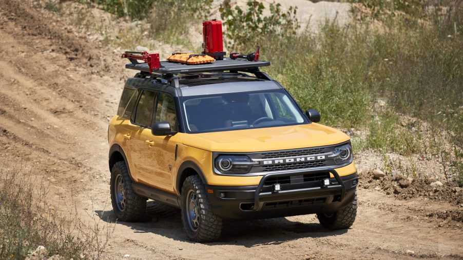 A yellow 2021 Ford Bronco Sport with a roof rack and bump guard travel a dirt road.