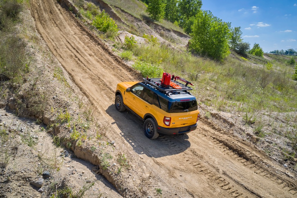 A yellow 2021 Ford Bronco Sport with a roof rack and bump guard travel a dirt road.