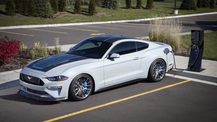 A white Ford Mustang Lithium is parked in a space next to a public charger.