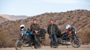 Ewan McGregor and Charley Boorman standing in front of their blue and orange Harley-Davidson LiveWires in the middle of the desert