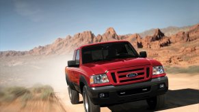 a red Ford Ranger pickup travels down a dirt road.