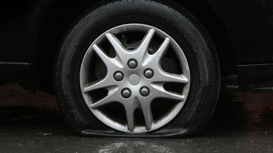 A flat tire on a car is seen on a wet pavement surface.
