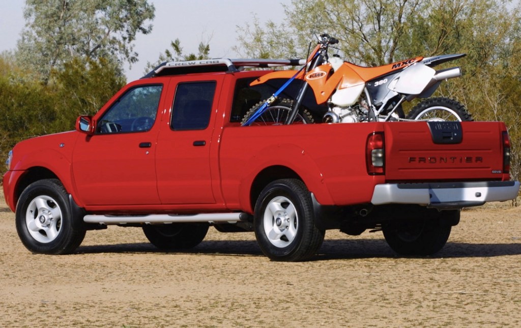 a red crew cab Nissan Frontier from the 2004 model year with a dirt bike in the back is a perfect example of one of the best used pickup trucks to buy
