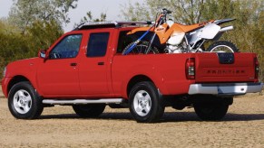 a red crew cab Nissan Frontier from the 2004 model year with a dirt bike in the back is a perfect example of one of the best used pickup trucks to buy