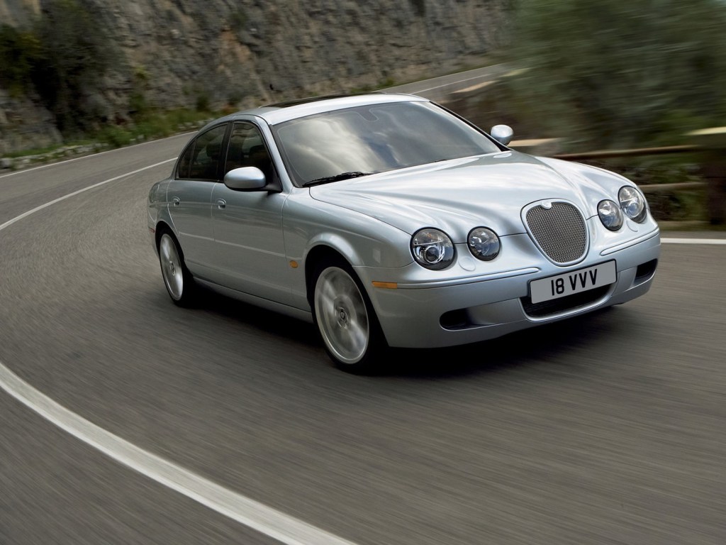 A silver Jaguar S-Type is pictured coming around a bend in the road.