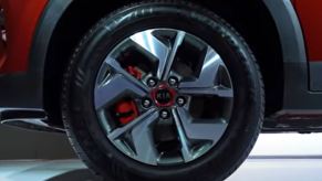 A red brake caliper is tucked in behind a silver wheel with a red accented center cap that says, Kia.