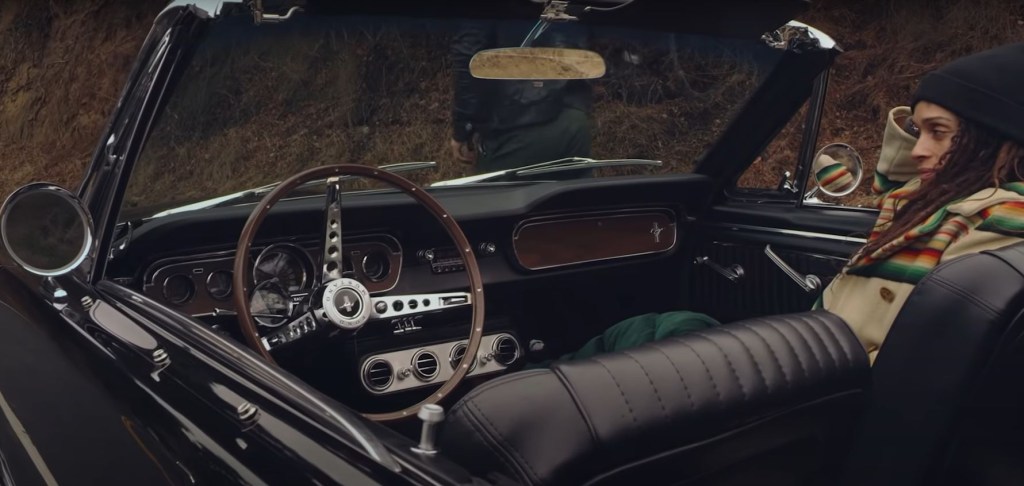 A classic black Mustang Convertible has its top down revealing Lisa Bonet in the passenger seat.