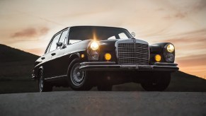 A black Mercedes 300SEL 6.3 in the desert at sunset with its lights on