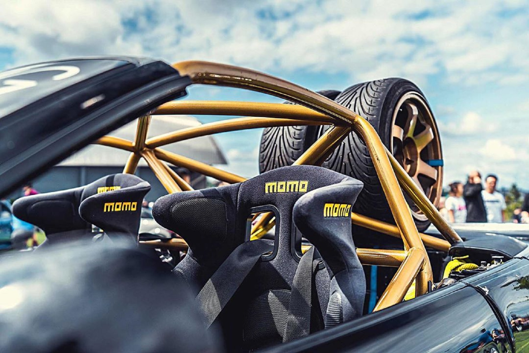 Black Momo racing seats with harnesses in a BMW E30 M3 with a gold roll cage