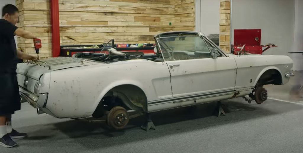 The shell of a 1965 Ford Mustang sits on tower jacks in a shop.