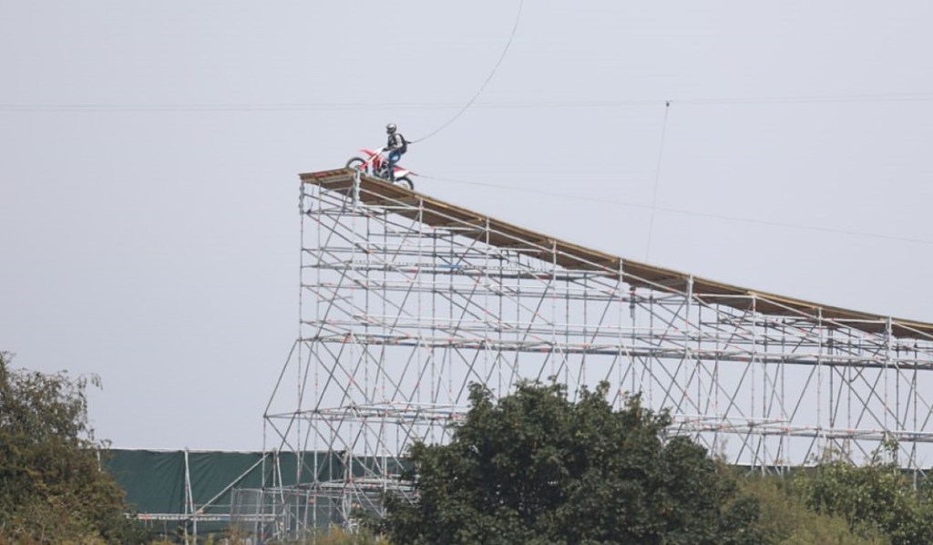 A stuntperson is on a motorcycle about to jump off a ramp.