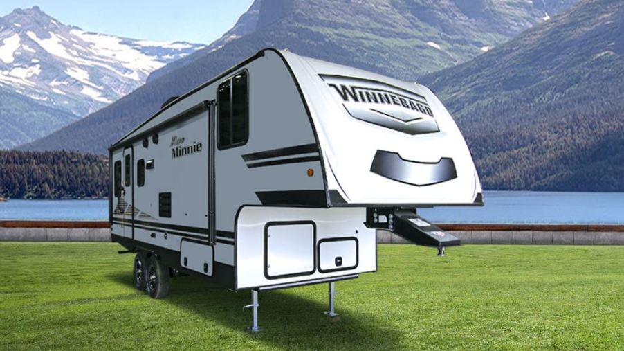 A white fifth wheel RV trailer is set in a snow-capped valley with a lake behind it.