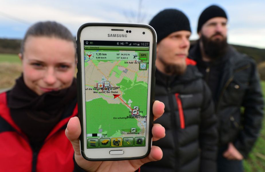 Amateur 'treasure hunters' Franziska Dennstedt (L-R), presenting her GPS capable smartphone and co-treasure hunters Sebastian Schwarz and Peter Scharf take part in an electronic treasure hunt near Klettbach, Germany, 29 January 2016. Geocaching is becoming increasingly popular in the state of Thuringia. According to the Thuringia's geocaching association, there are around 4,000 geocaching enthusiasts who regularly go on tour using their GPS to detect caches. Photo: Martin Schutt/dpa | usage worldwide (Photo by Martin Schutt/picture alliance via Getty Image