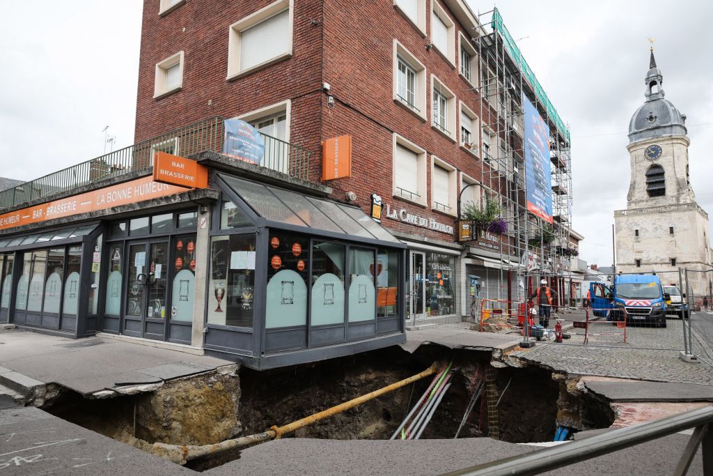 Construction workers stand near a sinkhole along a street in the city of Amiens, northern France, on August 13, 2019. - A five metres deep and ten metres wide sinkhole appeared in the centre of Amiens overnight on August 11, which the local municipal services believe could have been triggered by the collapse of a medieval cave in the vicinity. (Photo by DENIS CHARLET / AFP) (Photo credit should read DENIS CHARLET/AFP via Getty Images)