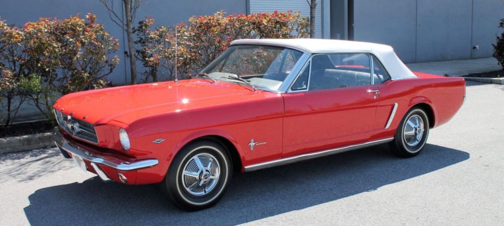 A classic red Ford Mustang convertible with a white top viewed from the front driver side. 