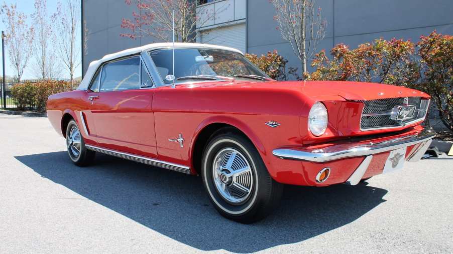 A classic red Ford Mustang convertible with a white top viewed from the front passenger side.