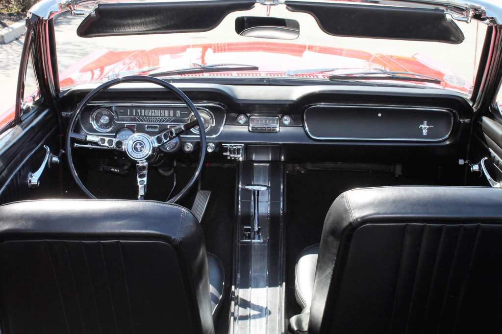 The black interior of a classic Ford Mustang is viewed from above the rear while the top is down.