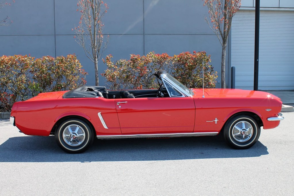 A classic red Ford Mustang convertible with the top down sits in front of a building.