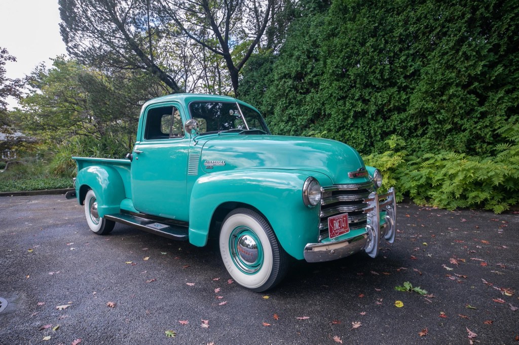 A teal 1951 Chevy 3100 truck on a hedge-lined driveway