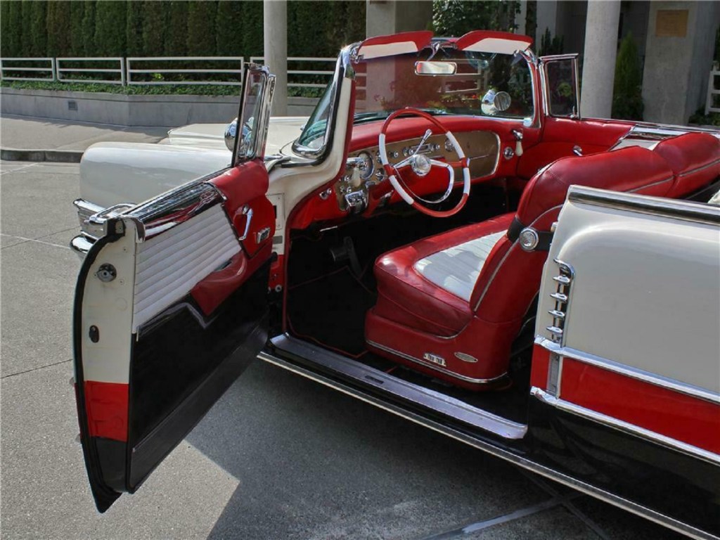 The red-and-white leather interior of a white-red-and-black 1955 Packard Caribbean seen through the open door