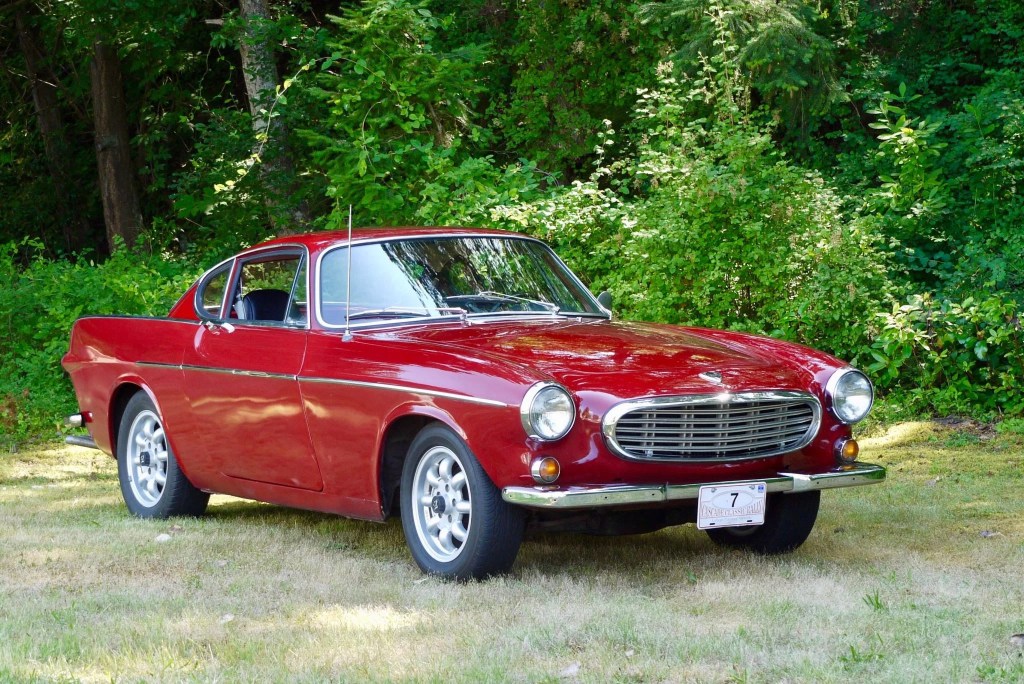 A red 1967 Volvo P1800S in front of a forest