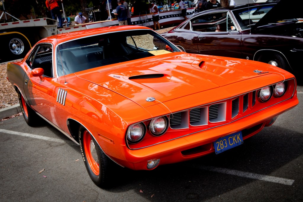 A classic red Plymouth Barracuda muscle car is viewed from the passenger front quarter side.