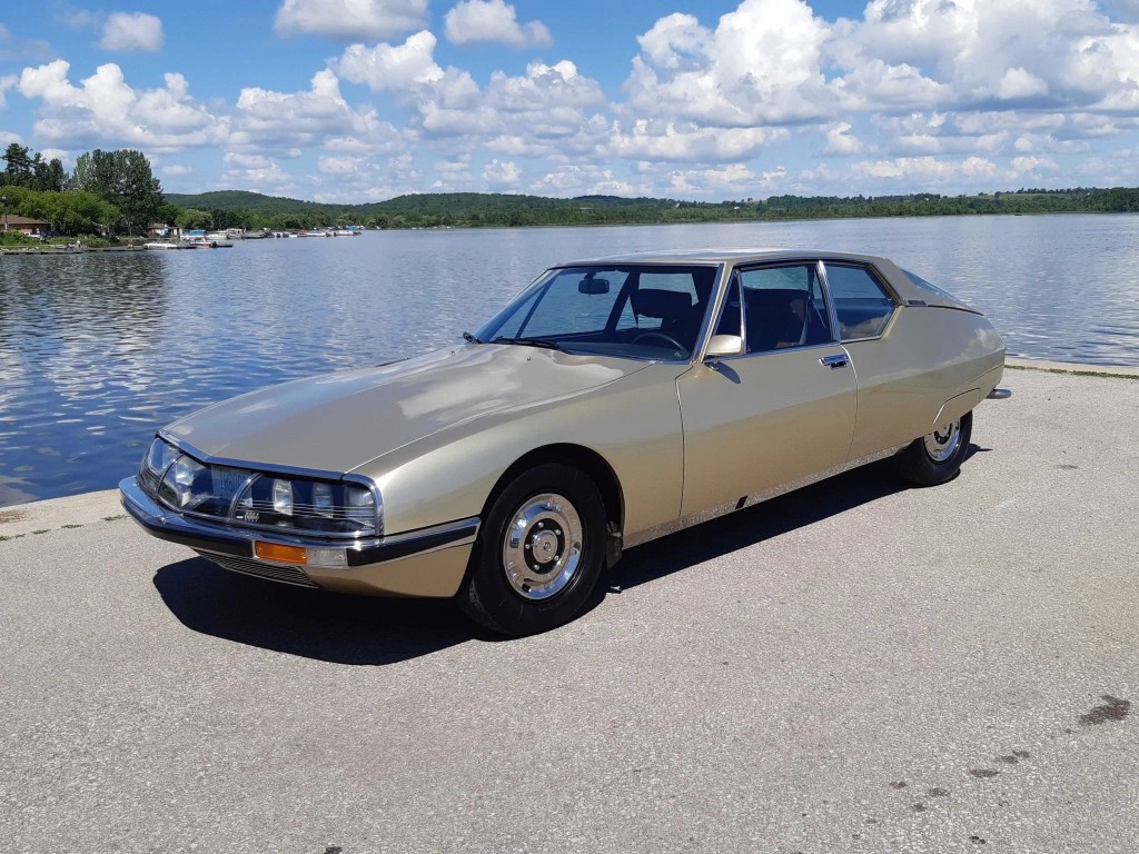 A gold 1972 Citroen SM in front of a lake