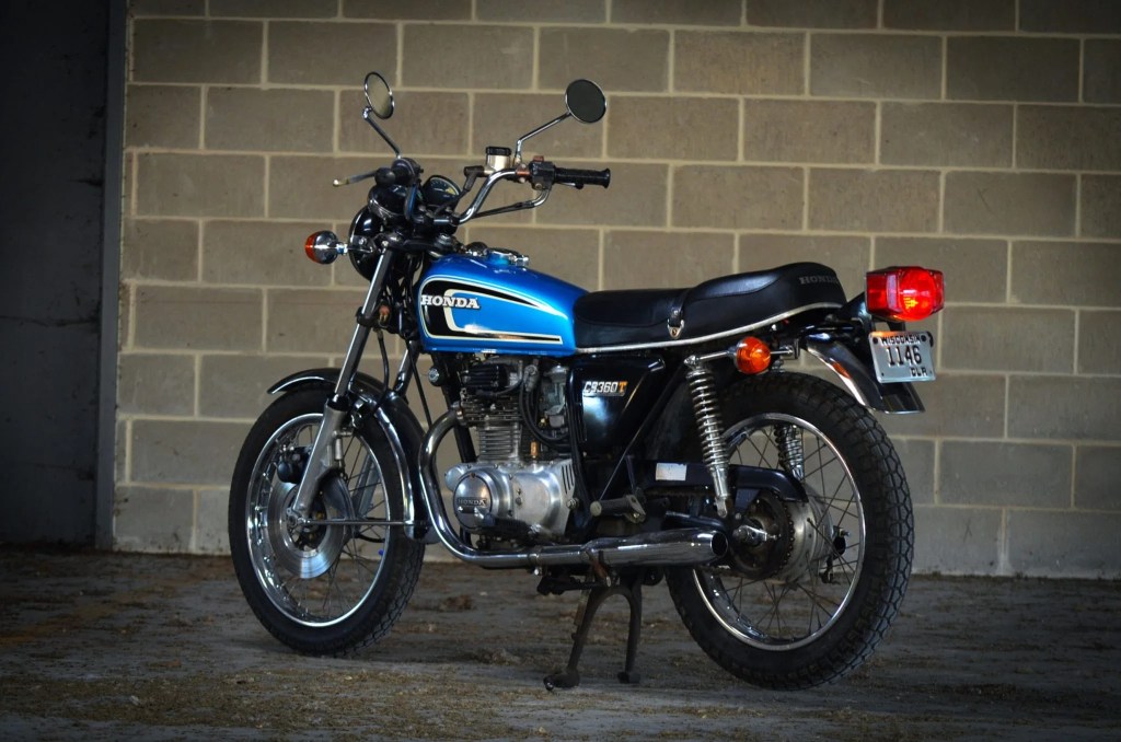 The rear 3/4 view of a blue 1975 Honda CB360T in a parking garage