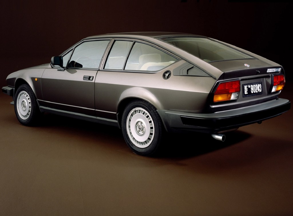 The rear-3/4 view of a gray 1980 Alfa Romeo GTV6 against a brown background
