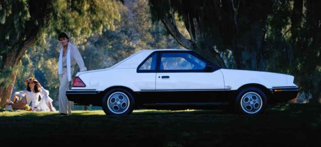 A white-and-black 1982 Ford EXP in a shady forest area