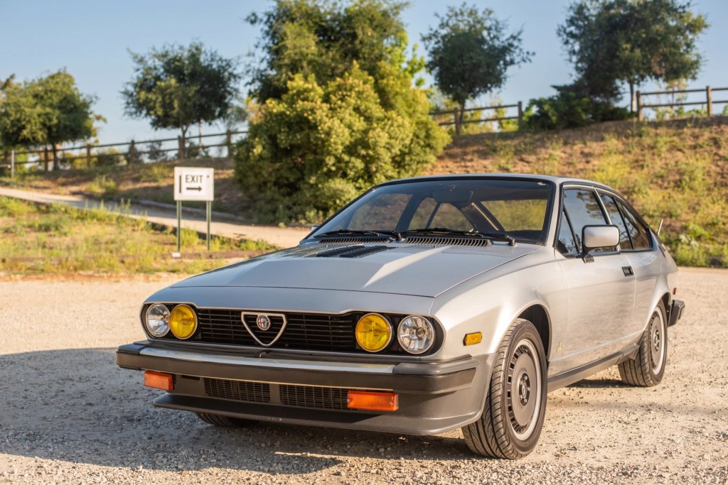 A silver 1983 Alfa Romeo GTV6 on a beach at sunset