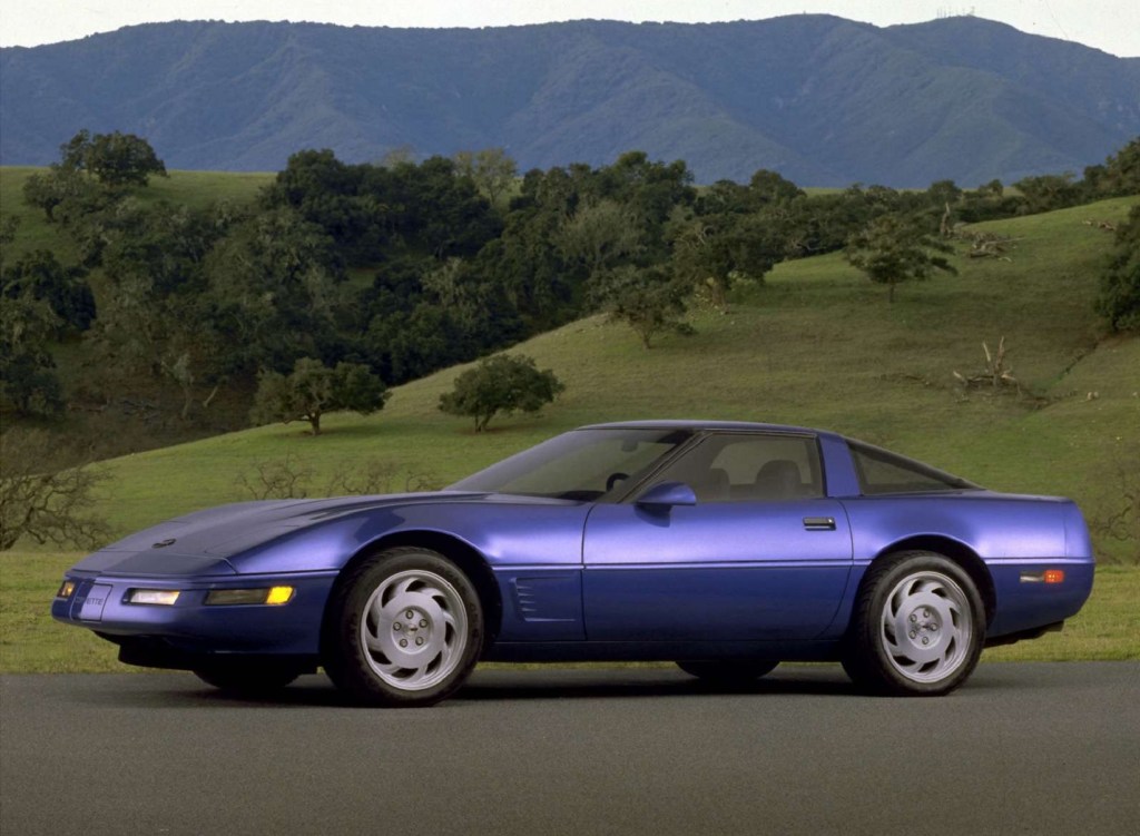 A blue 1983 Chevrolet C4 Corvette in front of some rolling green hills