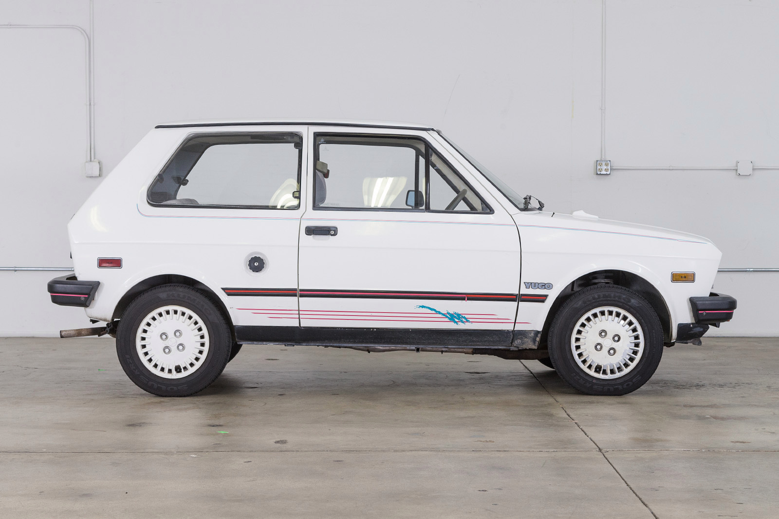 A small, white, hatchback profile-view of the Yugo.